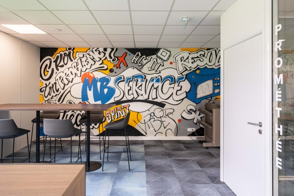 Création d'un espace informel chez MB ELECTRONIQUE avec papier peint artistique sur mesure, table haute et chaise haute.