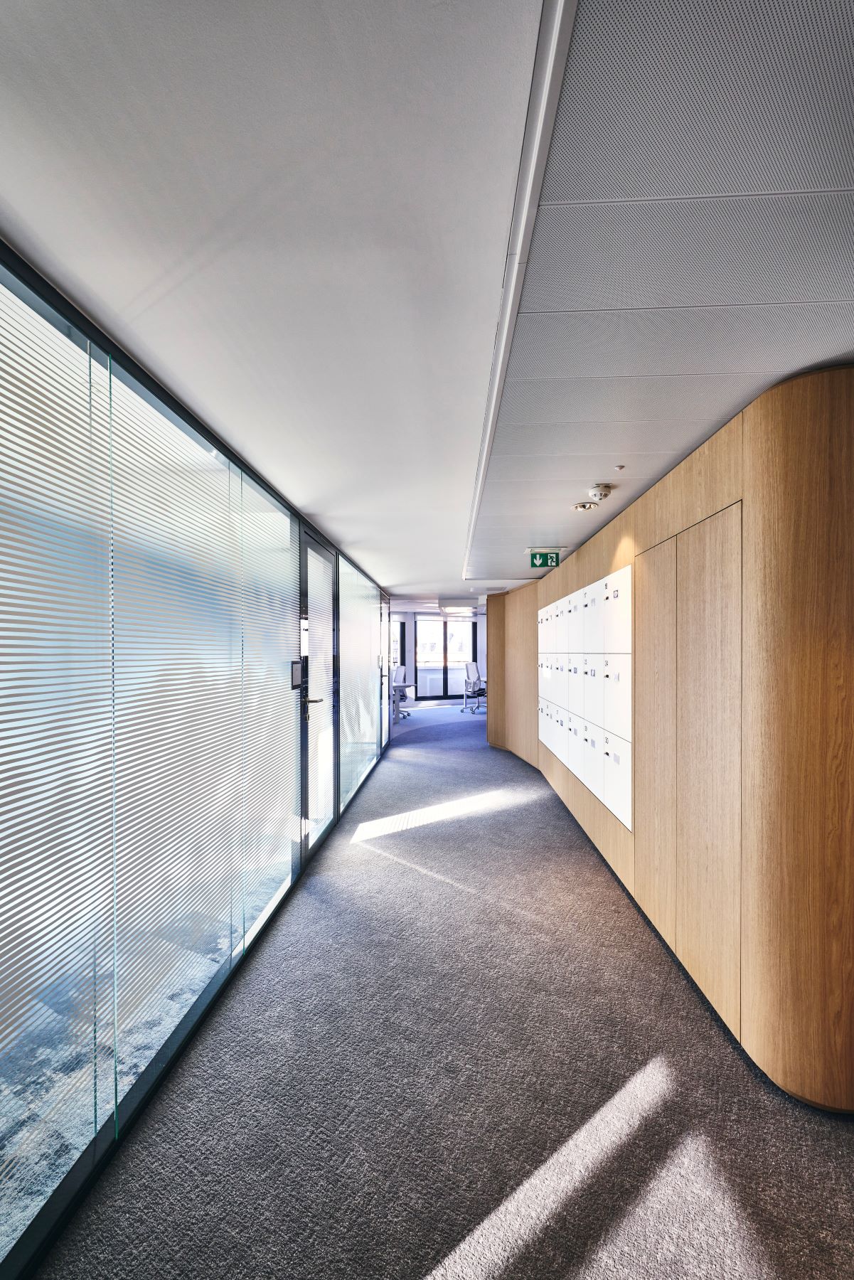 Perspective de la zone de circulation chez CCR avec agencement sur mesure pour intégration des casiers et d'une armoire, vitrophanie et moquette sobre.