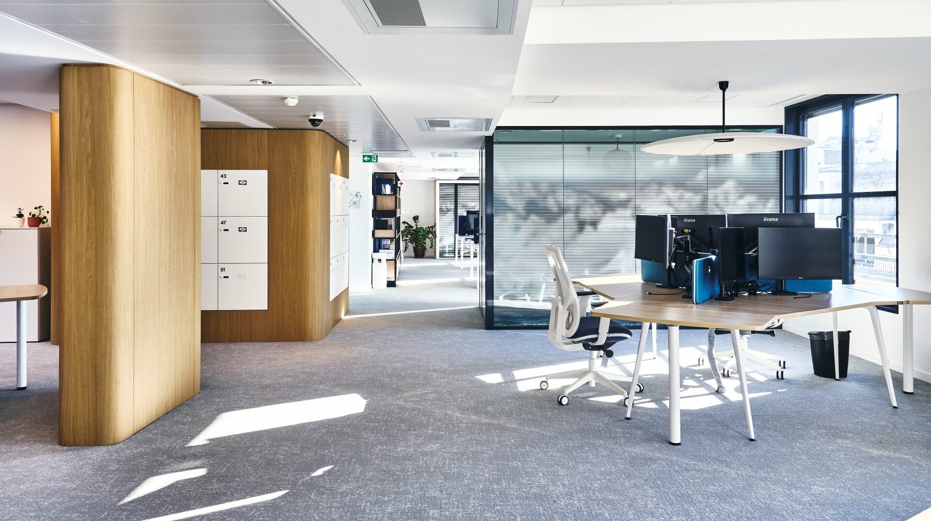 Aménagement d'un open-space chez CCR, avec bench de 3 personnes en trèfle, menuiserie sur mesure pour habillage du pilier, intégration des casiers en agencement sur mesure, salle de réunion en cloison double vitrage acoustique et vitrophanie, suspension luminaire absorbeur acoustique.