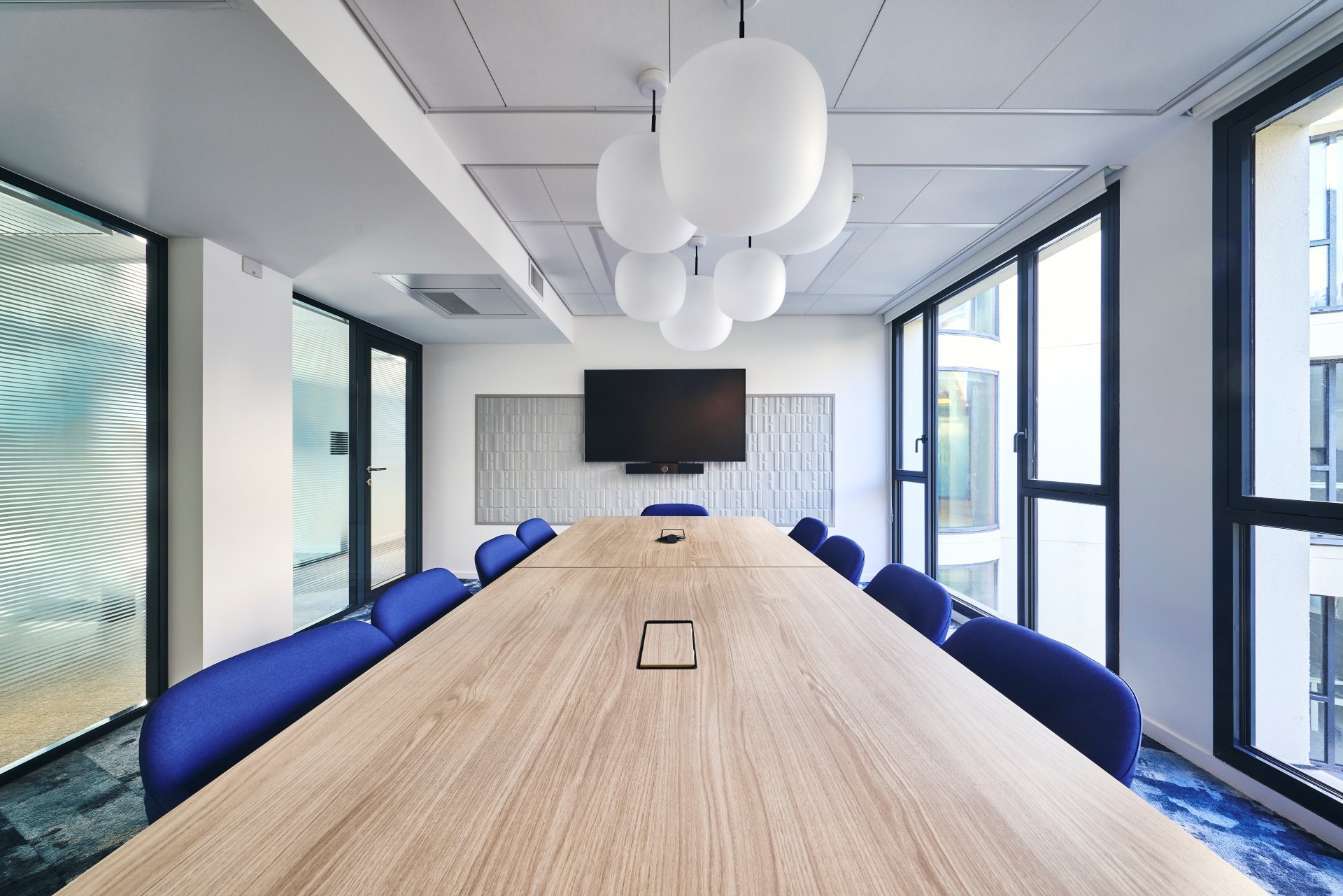 Aménagement d'une salle de réunion 10 personnes chez CCR, avec suspension luminaire globe, fauteuil confort et cloison double vitrage acoustique.