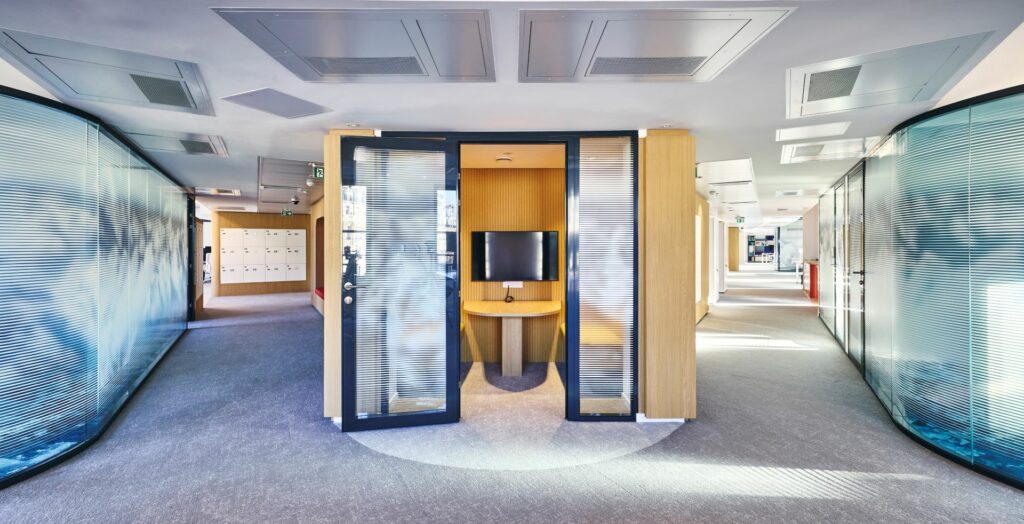 Aménagement de l'angle du bâtiment en box acoustique chez CCR, avec menuiserie sur mesure, panneaux acoustiques, banquette sur mesure et bloc porte vitrée acoustique.